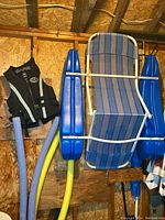 Full view of floating chair, black men's lifejacket, and two pool noodles hanging on a wooden wall.