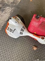 Side view of the Stihl FS 40 engine housing and attached red fuel canister on diamond plate floor