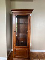 Front view of medium brown wood cabinet with glass door and two visible glass shelves inside plus a wooden lower door section, showing overall structure and condition.