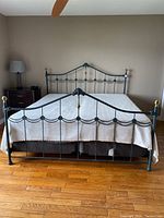 Full view of assembled dark green metal king size bed frame with mattress and bedding on hardwood floor