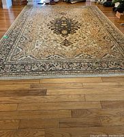 Full view of the large rectangular carpet on hardwood floor showing detailed floral and geometric patterns and borders.