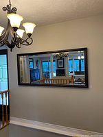 Front view of the large wall mirror mounted on a wall reflecting a chandelier and staircase.