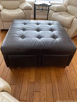 Front view of the brown leather ottoman showing button tufted top and two side drawers.