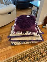 Stack of folded quilt and pillow shams topped by a plum rosette pillow