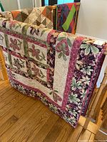 Quilt displayed hanging over a wooden railing showing the floral patchwork pattern and border.