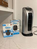 Two Thermacell Radius mosquito repellent products in packaging next to Sylvania silver vertical tower fan heater on a white table.