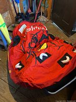 Folded red towable tube with black and yellow face design and multiple handles captured on floor among storage items.