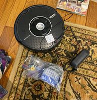 Black Roomba Pet Series vacuum on hardwood floor with charger and bagged accessories visible