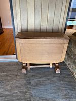 Folded table viewed from front against wall showing drop leaves folded down and base structure