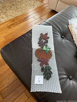 Stained glass autumn decoration placed on bubble wrap on a leather couch, showing pumpkin and fall leaves design.