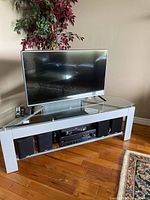 LG television and Yamaha stereo components with speakers on white glass and metal TV stand on hardwood floor.