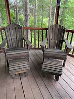 Two weathered wood Adirondack chairs with matching wooden ottomans on a porch.