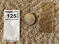 Photo of the coin face showing heraldic eagle and denomination with a MaxSold paper tag and coin plastic holder beside it.