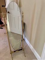 Front angled view showing the oval mirror on brass base with decorative finials at top corners.