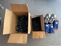 Open cardboard boxes showing green wired Christmas string lights with frosted white bulbs, red bulbs, and additional boxed sets.