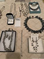 Full assortment of costume jewelry laid out on a beige carpet, showing all items in the lot including multiple necklaces, earrings, a bracelet, and a watch.