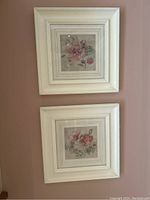 Two signed Blum framed floral prints with white ornate frames hanging on wall.