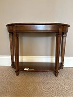 Front view of wooden demi-lune hall table with carved details on legs and paneled apron, showing open lower shelf.