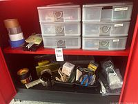 Plastic drawer storage units labeled hose parts, screws, and tape on red shelf, various hardware items in trays below