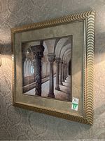 Frontal view of the framed artwork showing the column scene and ornate gold-toned frame with textured beige matte.