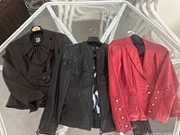 Three ladies leather jackets displayed on glass table: brown, black, and red jacket