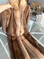 Close-up view of demi buff mink fur coat with fox fur collar and trim laid on a glass table showing texture and color.