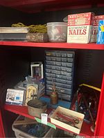 Multi-drawer red caddy showing numerous small parts drawers with various hand tools, blue and red boxes, and an oil can