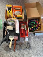 Complete view of paint tray loaded with paint rollers, brushes, scraper, and lead weights alongside box of bungee cords