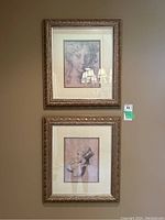 Two framed prints hung on a wall, both classical female portraits in gold-tone ornate frames with mats.