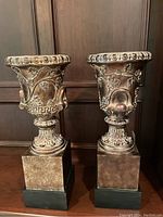 Pair of brown and black Italian style urns with grapevine motif against wooden wall