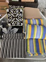 Overview of all cushions and fabric pieces showing three different styles and fabrics incl. square patterned, striped elongated, and plain tan cushions.