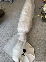 Long patio umbrella covered in a sheer protective sleeve, lying horizontally on a granite countertop with the base stand attached.