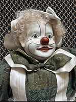 Close-up of the bisque porcelain clown face with white makeup, red nose, detailed painted features, curly blonde hair and white bow.
