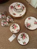 Top view showing a stack of dinner plates, salad plates, dessert plates, tea cups, and saucers all decorated with pink rose patterns and gold accents.