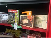 Shelf with Yard Gard electronic pest chaser, Mastercraft Sabre Saw boxed, Black & Decker finishing sander boxed, drill bits packaging, and extension cords below.