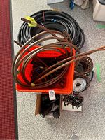 Orange bucket containing coiled copper pipes and hoses, black hoses coiled around the bucket, box below containing fittings.