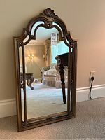 Full view of the ornately framed wall mirror with its reflective glass surface showing light room reflection.