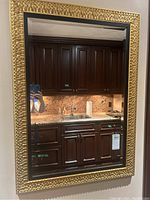 Full view of the rectangular mirror showing gold textured frame and beveled glass reflecting a kitchen area.