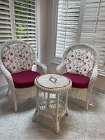 Front view of two white wicker chairs with cushions and matching table