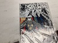 Front cover of Spawn comic issue #10 showing black and white art with character and chains. Sealed in protective plastic.