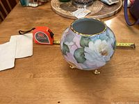 Photo showing the side of the round vase decorated with white roses and green leaves in Art Nouveau style, along with a tape measure for scale.