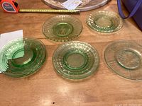 Seven green Depression glass plates on wooden table showing variety of patterns and textures