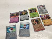 Overview of all eight Pokémon cards arranged on a flat surface, showing fronts including shiny holographic artwork and Trainer cards.