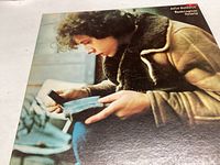Front cover close-up showing a young man in a brown shearling jacket looking at an item in his hand, with Arlo Guthrie Washington County text.