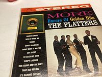 Front cover of vinyl record 'More Encore Of Golden Hits The Platters' showing colorful design with the band and track list