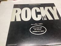 Front cover of the Rocky Original Motion Picture Score vinyl record showing large white 'ROCKY' text and mention of hit single 'Gonna Fly Now'.