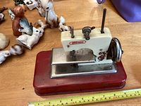 Full side view of the toy sewing machine showing red base, white upper section with decals, and hand crank
