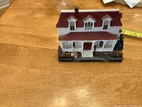 Front view of the Victorian-style miniature house figurine on a wood surface with a measuring tape nearby for scale.