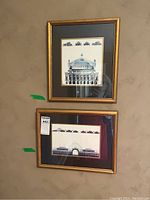 Two framed architectural prints hanging on a beige wall, featuring classical building elevations with gold frames and glass coverings.