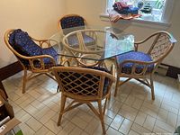 Four bamboo chairs arranged around a glass dining table, showing chair style, cushion design and general condition.